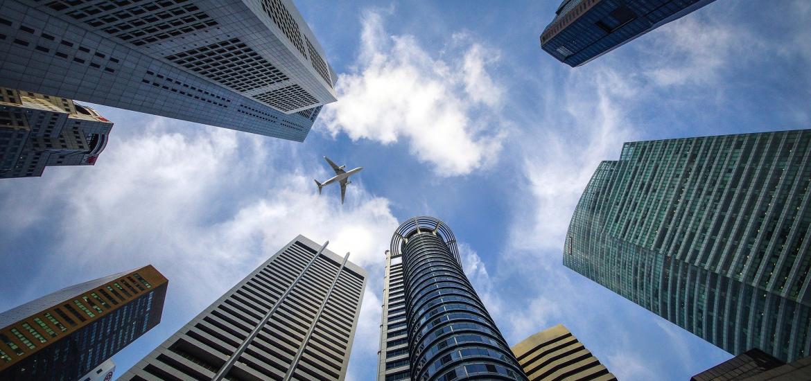 Skyscrapers looking up into the blue sky with an airplane in the middle